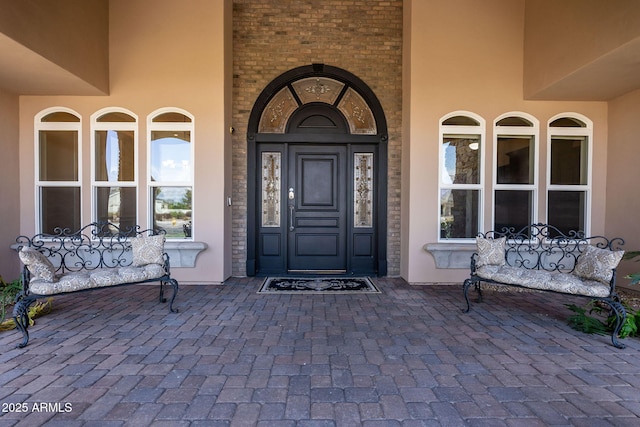 view of exterior entry with stucco siding, brick siding, and covered porch