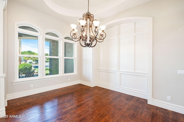 spare room featuring a chandelier, baseboards, and dark wood-type flooring