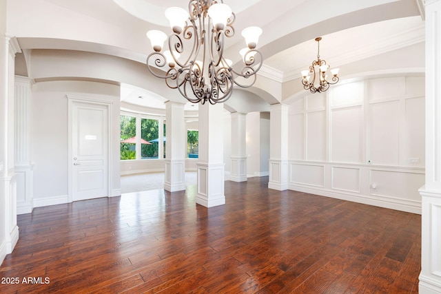 unfurnished dining area with a decorative wall, an inviting chandelier, dark wood-style flooring, and arched walkways