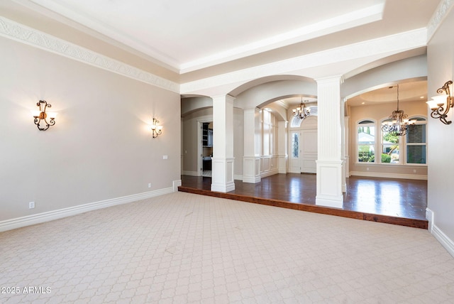 carpeted empty room featuring baseboards, a notable chandelier, arched walkways, and ornate columns