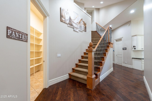 staircase with wood finished floors, built in features, baseboards, a towering ceiling, and recessed lighting
