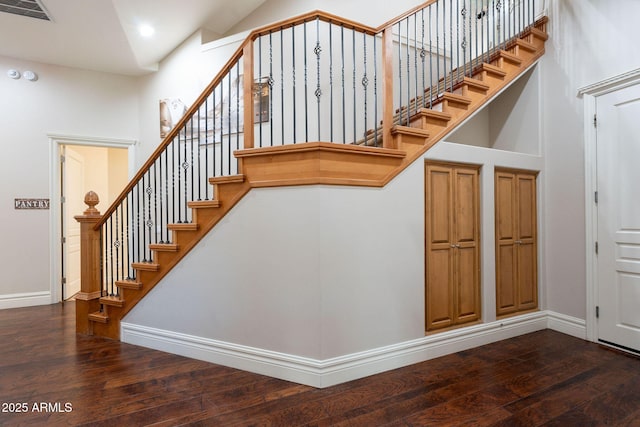staircase with baseboards, hardwood / wood-style floors, visible vents, and a high ceiling