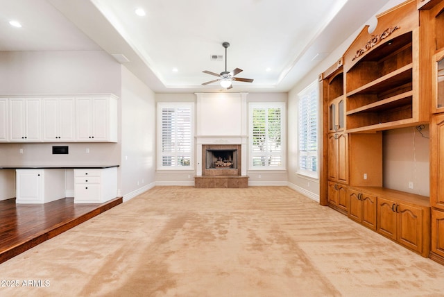unfurnished living room featuring a ceiling fan, a fireplace, a raised ceiling, and carpet floors
