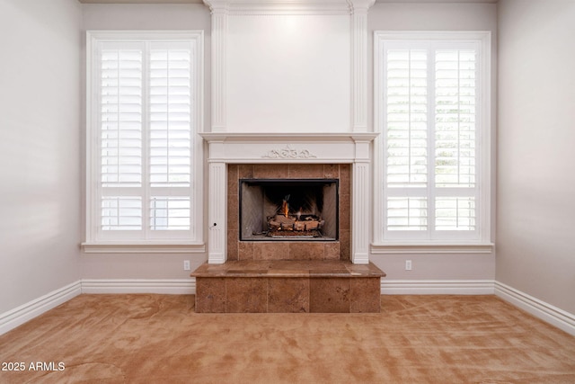 unfurnished living room featuring baseboards, a tile fireplace, a healthy amount of sunlight, and carpet
