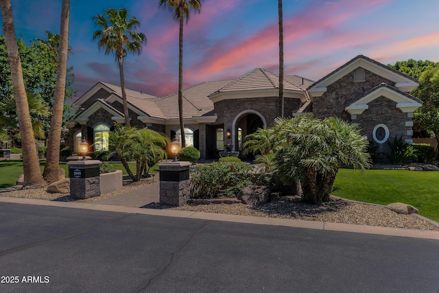view of front of house featuring a tile roof, stone siding, and a yard