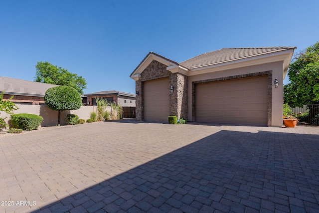 view of front of house with a tile roof, fence, an attached garage, and decorative driveway