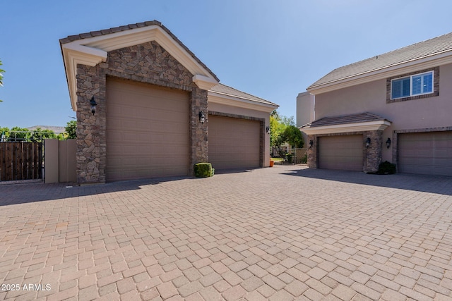 view of front of home with stone siding, a tiled roof, stucco siding, fence, and decorative driveway
