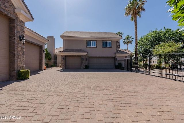 view of front facade featuring fence, decorative driveway, a garage, stucco siding, and stone siding