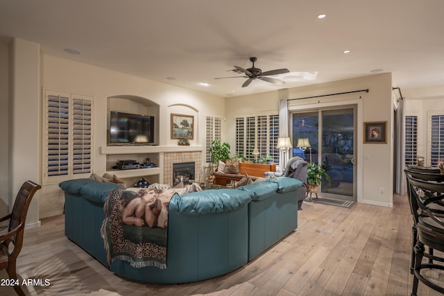 living room featuring ceiling fan, light wood-type flooring, and a tile fireplace