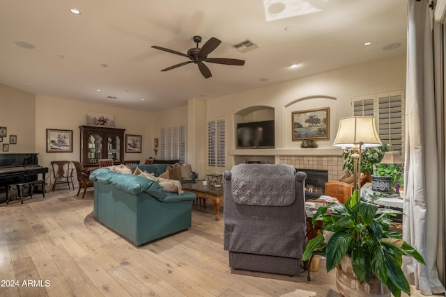 living room with a tiled fireplace, ceiling fan, and light wood-type flooring