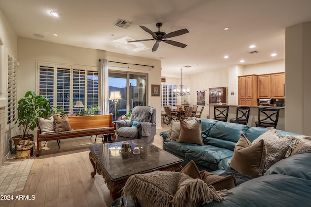 living room featuring ceiling fan with notable chandelier and light hardwood / wood-style flooring