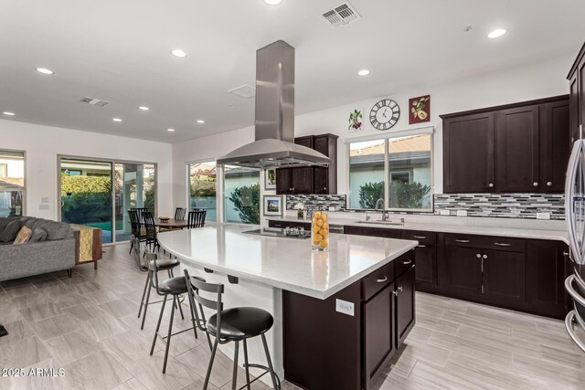 kitchen featuring sink, a breakfast bar, a center island, black electric stovetop, and island exhaust hood