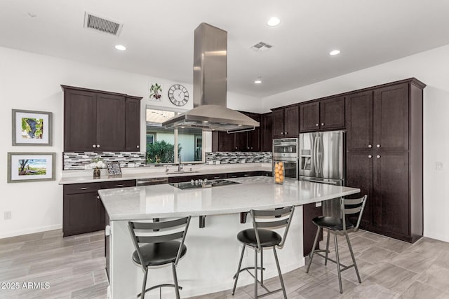 kitchen featuring appliances with stainless steel finishes, a breakfast bar, island range hood, sink, and light stone counters