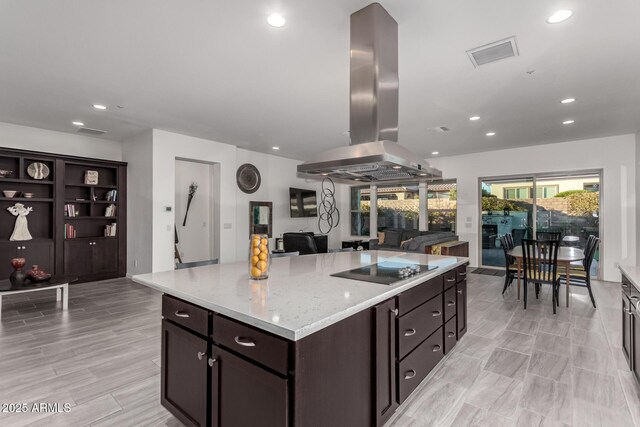 kitchen featuring a kitchen island, island exhaust hood, light stone countertops, dark brown cabinets, and black electric cooktop