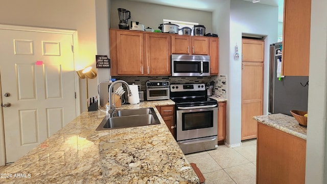 kitchen featuring backsplash, light stone counters, sink, and appliances with stainless steel finishes