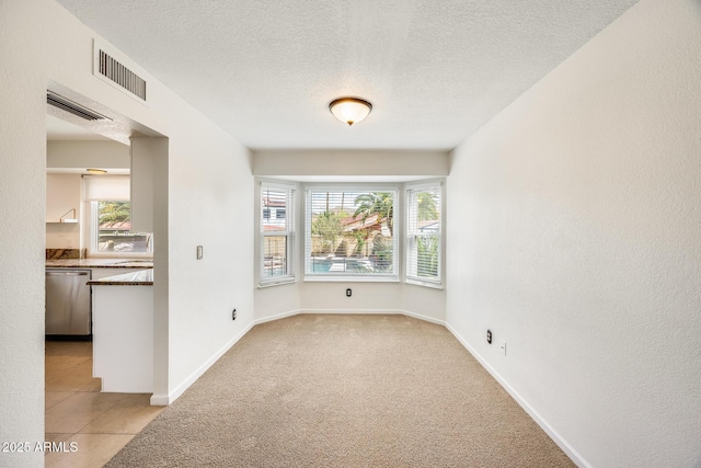 empty room with visible vents, light carpet, a textured ceiling, and baseboards