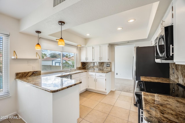 kitchen with a sink, light stone counters, white cabinetry, appliances with stainless steel finishes, and a peninsula