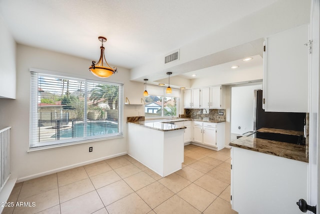 kitchen featuring light tile patterned floors, visible vents, a peninsula, white cabinetry, and backsplash