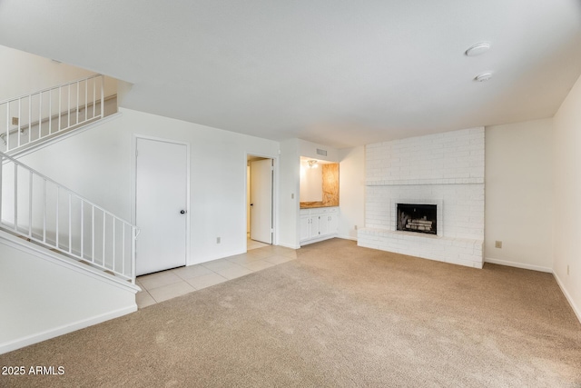 unfurnished living room with stairway, a brick fireplace, baseboards, and carpet floors