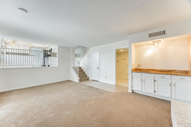 unfurnished living room featuring stairway, baseboards, visible vents, a sink, and light carpet