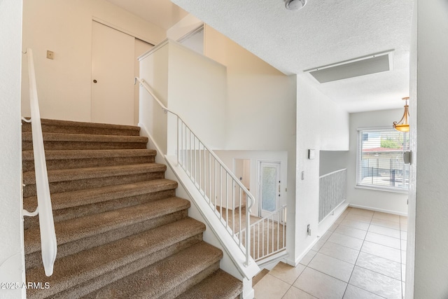 stairs with tile patterned flooring, baseboards, and a textured ceiling