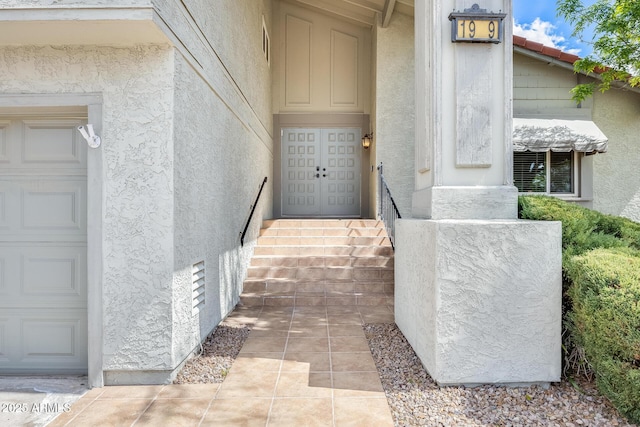 doorway to property with a garage, visible vents, and stucco siding