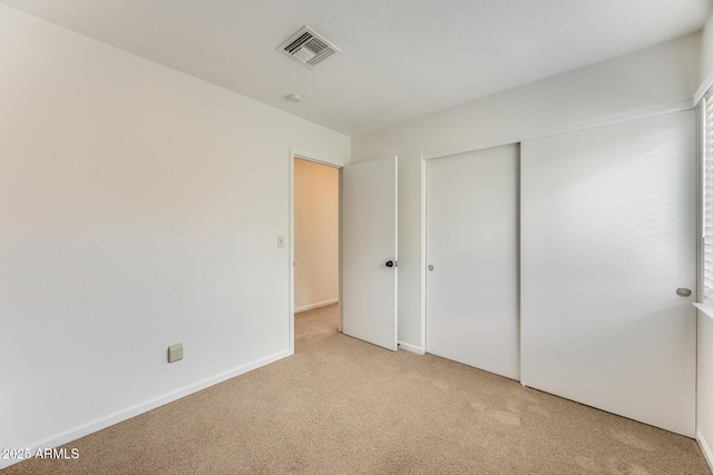 unfurnished bedroom with light carpet, visible vents, baseboards, and a closet