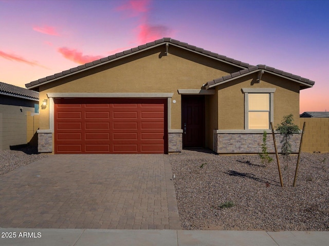 ranch-style house featuring stucco siding, a tile roof, decorative driveway, stone siding, and a garage