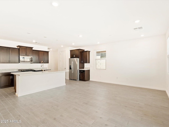 kitchen with visible vents, an island with sink, stainless steel appliances, dark brown cabinets, and light wood-type flooring