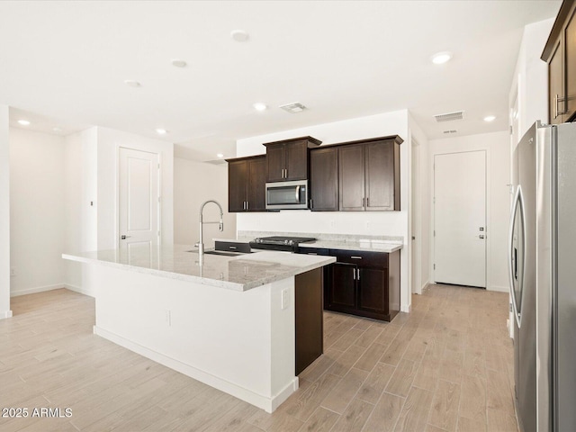 kitchen featuring visible vents, a center island with sink, light wood-style flooring, stainless steel appliances, and a sink