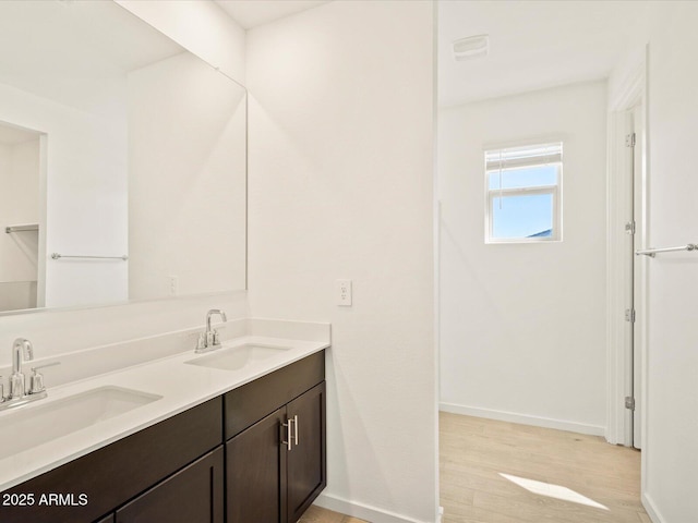 bathroom with double vanity, wood finished floors, baseboards, and a sink