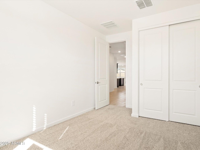 unfurnished bedroom featuring light colored carpet, visible vents, a closet, and baseboards