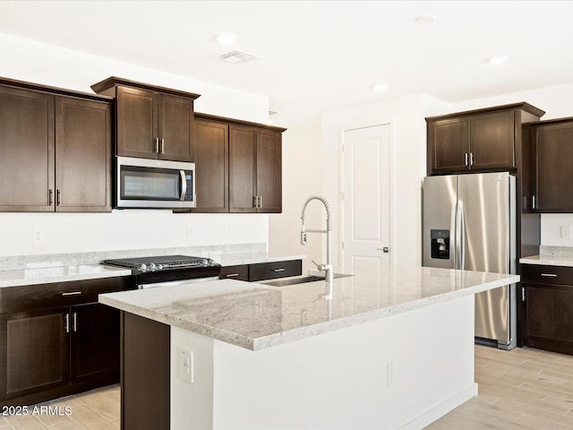 kitchen featuring light wood-type flooring, a sink, appliances with stainless steel finishes, light stone countertops, and dark brown cabinets