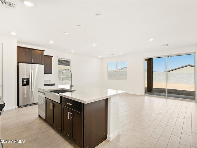 kitchen featuring light stone counters, visible vents, wood finish floors, a sink, and appliances with stainless steel finishes