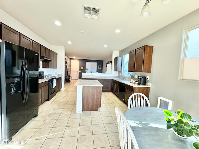 kitchen with dark brown cabinetry, light tile patterned flooring, kitchen peninsula, black appliances, and a center island