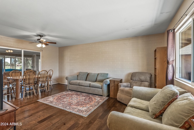 living room with brick wall, dark wood-type flooring, and ceiling fan