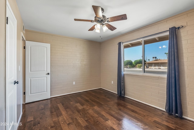 empty room with brick wall, ceiling fan, and dark hardwood / wood-style flooring