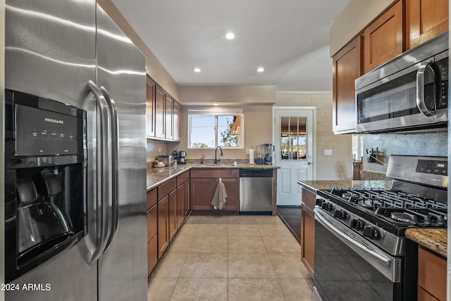 kitchen with appliances with stainless steel finishes, sink, stone counters, and light tile patterned floors