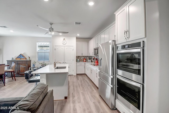 kitchen featuring white cabinetry, an island with sink, sink, decorative backsplash, and stainless steel appliances