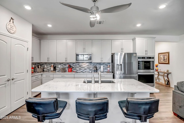 kitchen featuring sink, a kitchen island with sink, light stone counters, light hardwood / wood-style floors, and stainless steel appliances