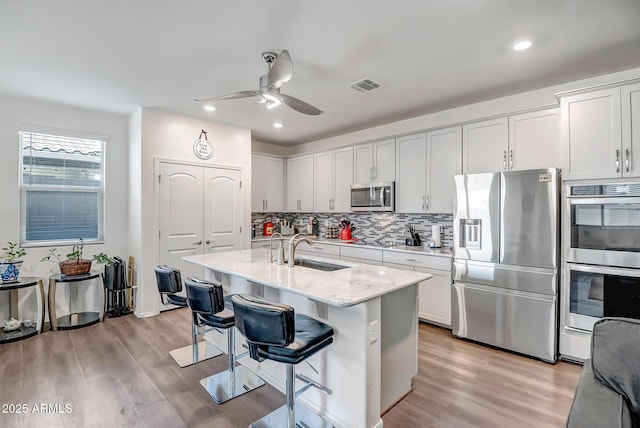 kitchen with sink, appliances with stainless steel finishes, a kitchen breakfast bar, an island with sink, and white cabinets