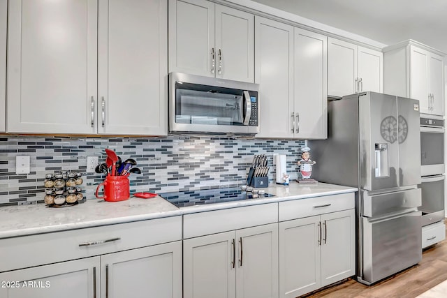 kitchen featuring appliances with stainless steel finishes, white cabinetry, tasteful backsplash, light stone counters, and light hardwood / wood-style floors