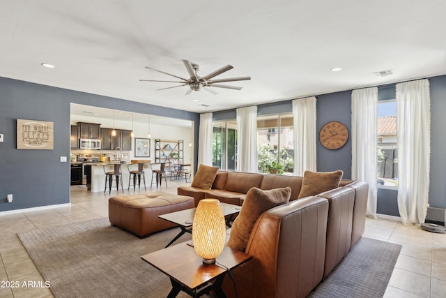 living area with light tile patterned floors, ceiling fan, and baseboards