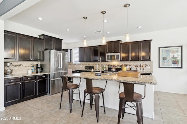 kitchen with appliances with stainless steel finishes, decorative backsplash, a breakfast bar, hanging light fixtures, and recessed lighting