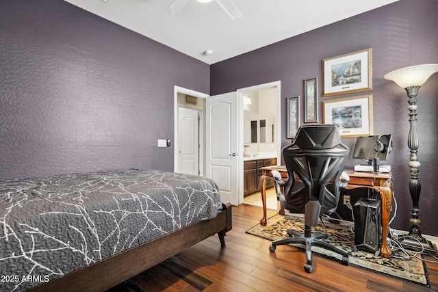 bedroom featuring wood-type flooring, a textured wall, ensuite bath, and ceiling fan