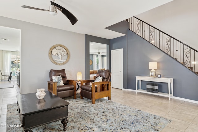 tiled living area with ceiling fan, stairway, and baseboards