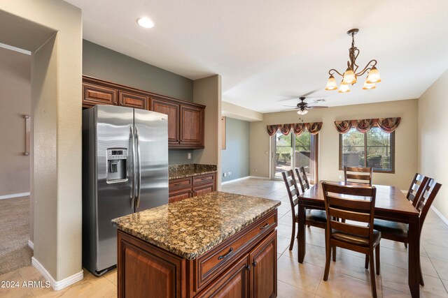 kitchen with stainless steel refrigerator with ice dispenser, dark stone countertops, pendant lighting, light tile patterned floors, and ceiling fan with notable chandelier