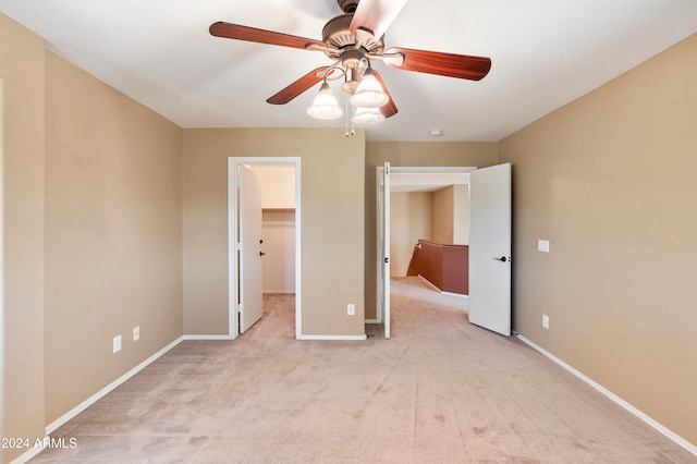 unfurnished bedroom featuring light carpet, a walk in closet, a closet, and ceiling fan