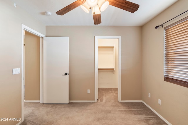 unfurnished bedroom with light colored carpet, a walk in closet, a closet, and ceiling fan