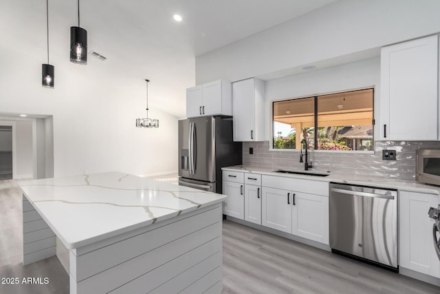 kitchen featuring pendant lighting, stainless steel appliances, a kitchen island, white cabinetry, and sink